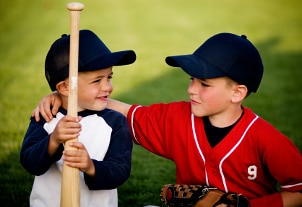 Brothers holding baseball equipment outside