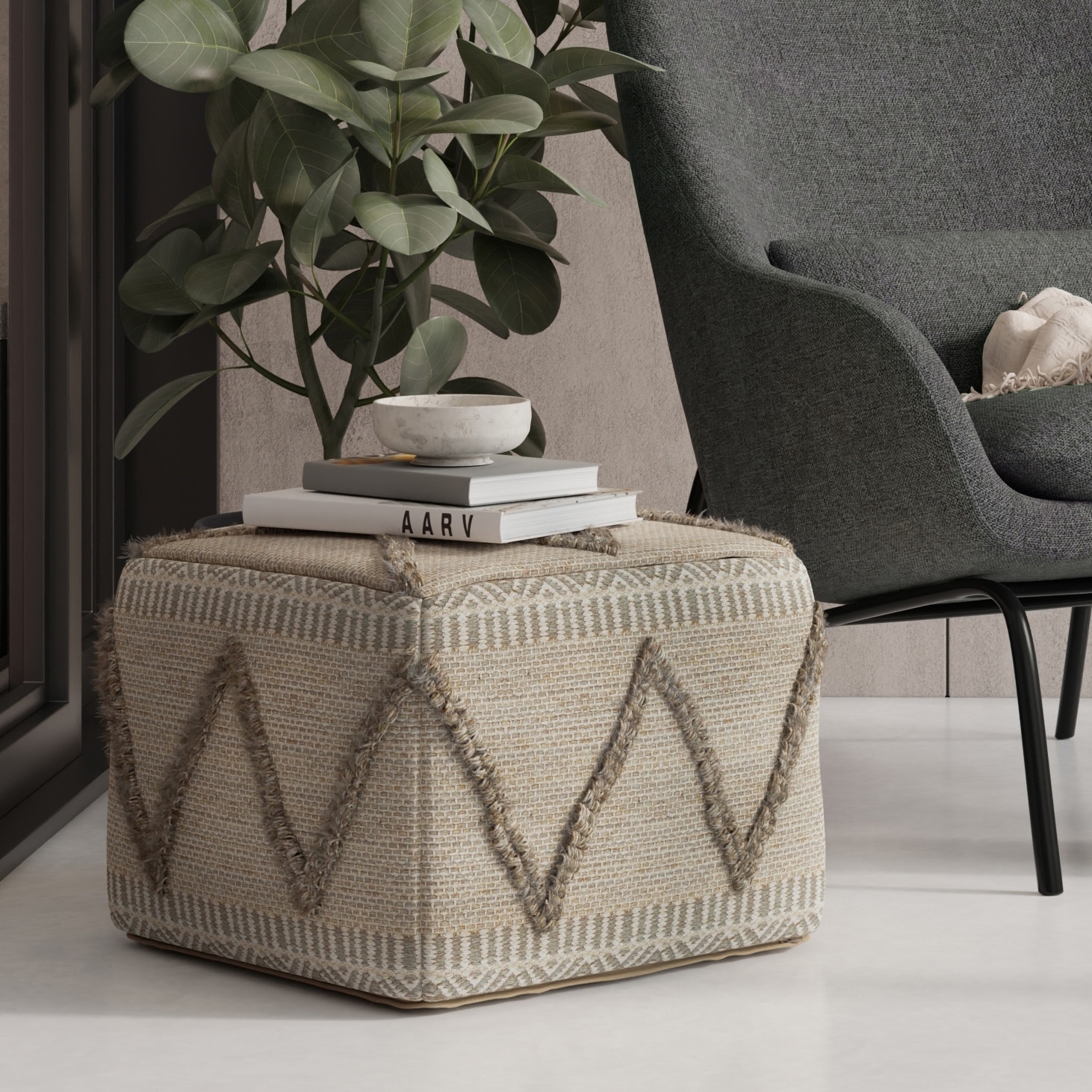 Beige textured pouf with geometric stitched pattern sits in a modern living room next to a gray chair and plant, with books on top