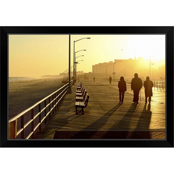 "Three people walking down boardwalk near beach at sunset." Black Framed Print