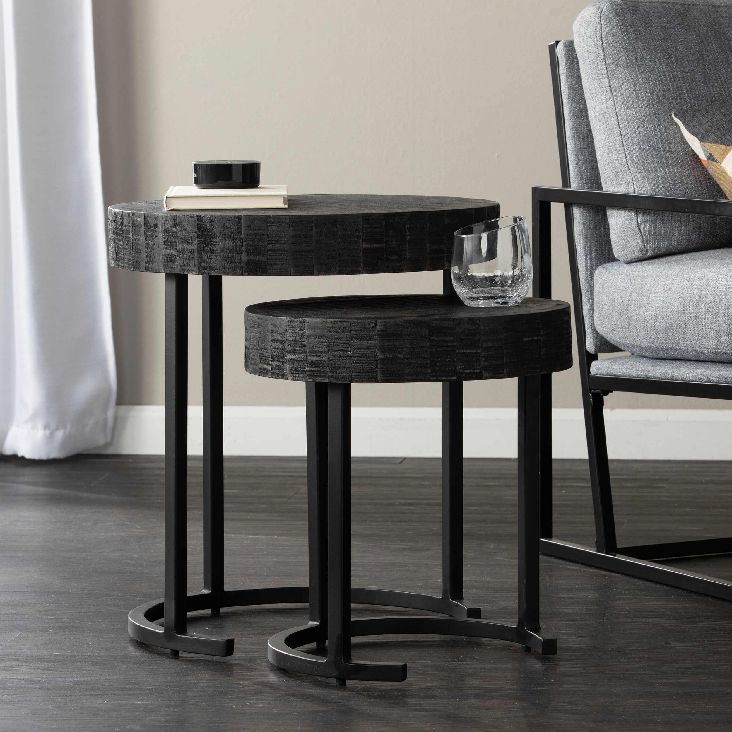 Two black nesting end tables with round tops, set beside a chair and glass tumbler on the larger table; living room setting.