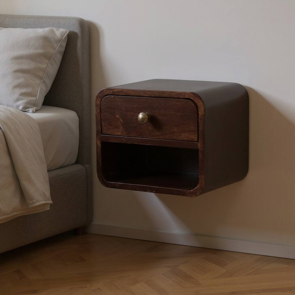A wall-mounted bedside table with a rounded rectangular open shelf below a small drawer, attached to a bedroom wall next to a bed.