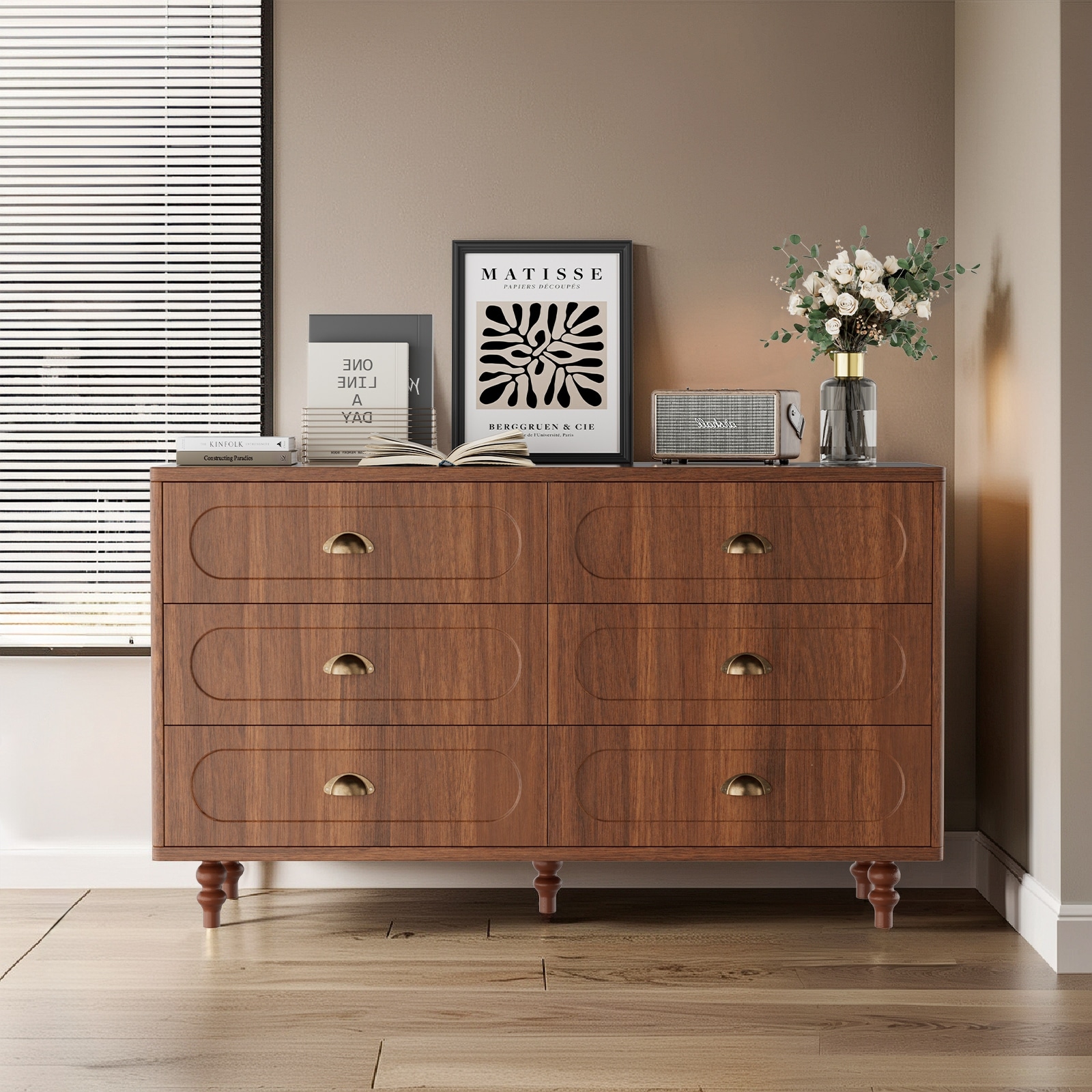 The same wooden dresser with decor on top including framed art, a small tree, books, a vase, and a vintage radio