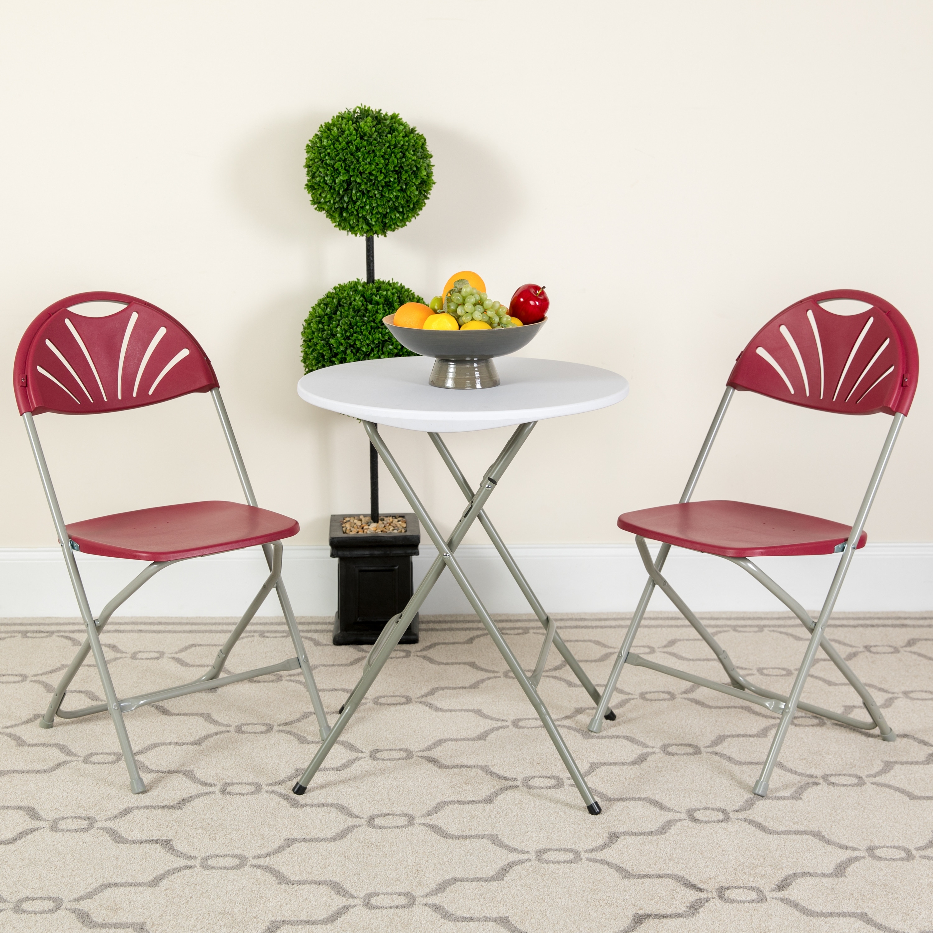 Two gray foldable chairs facing a small round white table with a black floor lamp behind; table has cards spread on it.