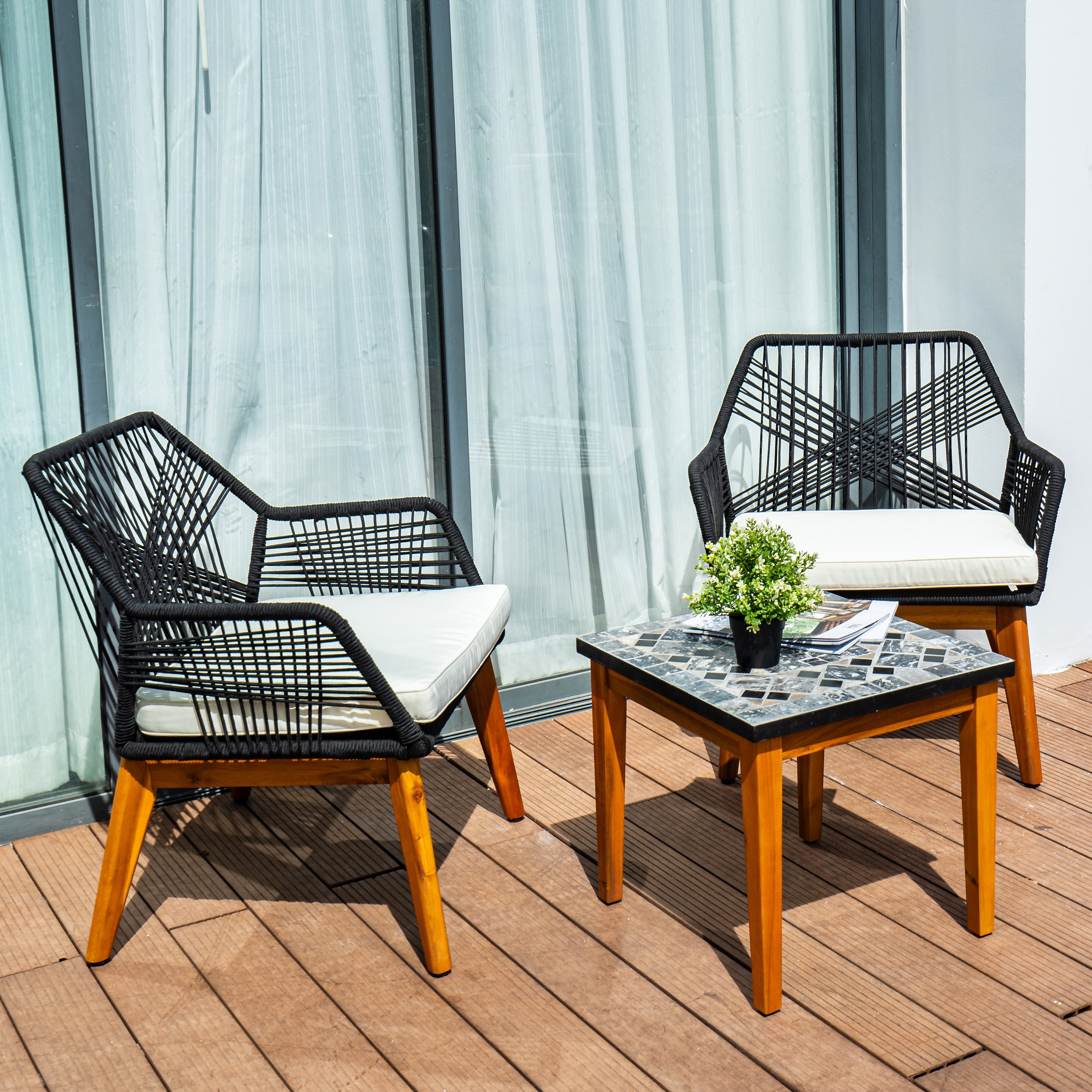 Two black woven chairs with white cushions and a small square table with a mosaic top on a wooden deck