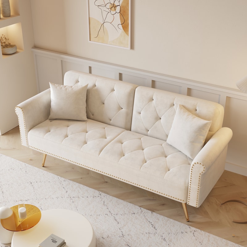 A 69.7-inch-long sofa bed covered in beige velvet fabric, featuring nail head trim and accompanied by a matching throw pillow