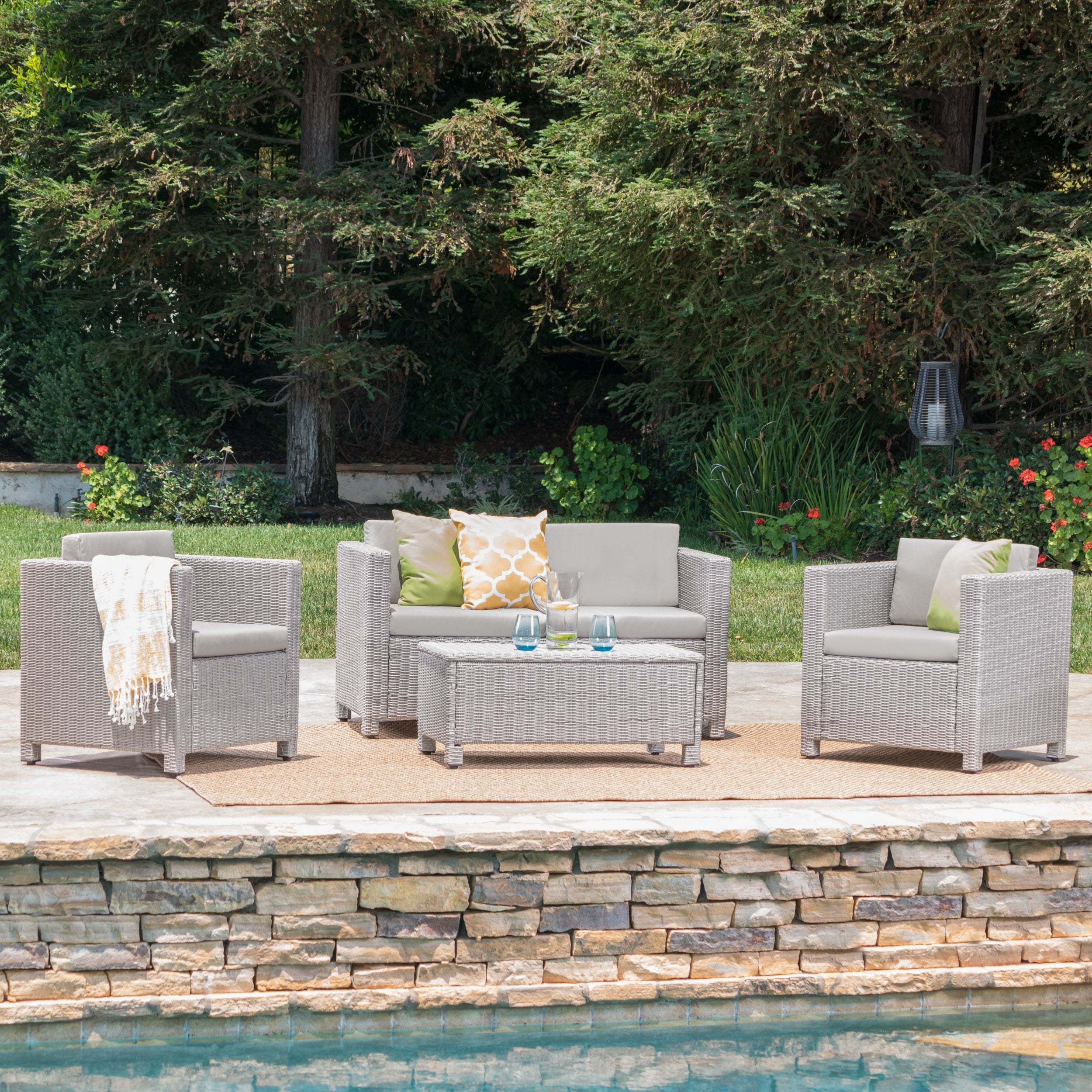 Outdoor wicker furniture set arranged on patio with trees in background, includes sofa, two chairs, and central table
