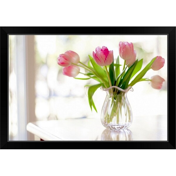 "Ruffled pink glass vase filled with soft, pink tulips in front of window" Black Framed Print