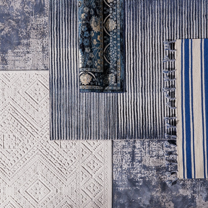 A display of layered area rugs of different patterns in shades of blue.