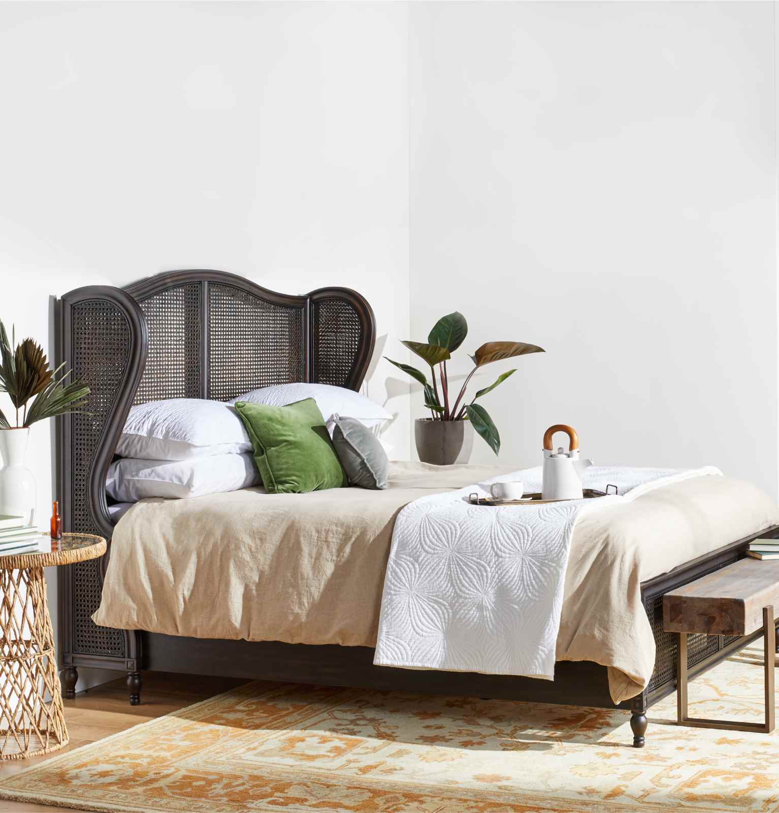 A made-up bed with a winged wicker headboard and a tray with tea on top available online at Overstock