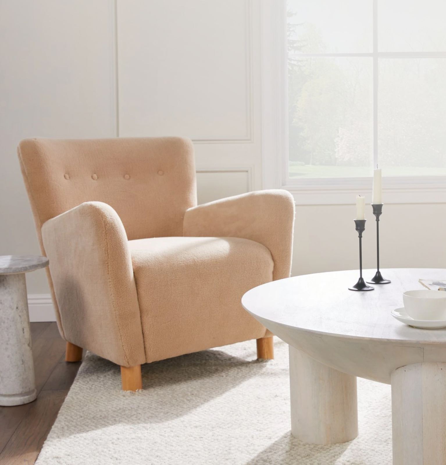A peach-colored accent chair is pictured with a white marble side table and matching coffee table..