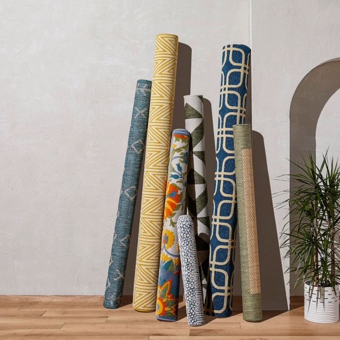 Assorted rugs rolled up leaning against grey wall.