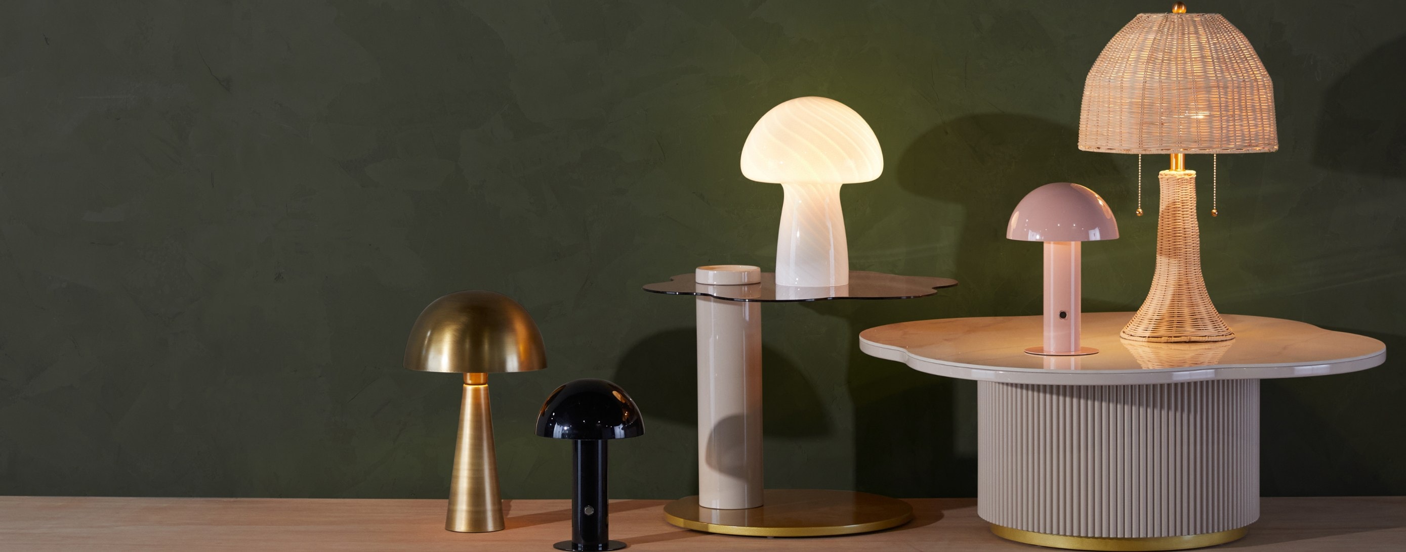 Several table lamps with dome-shaped shades on the floor and on a table in front of a green wall available online at Overstock.
