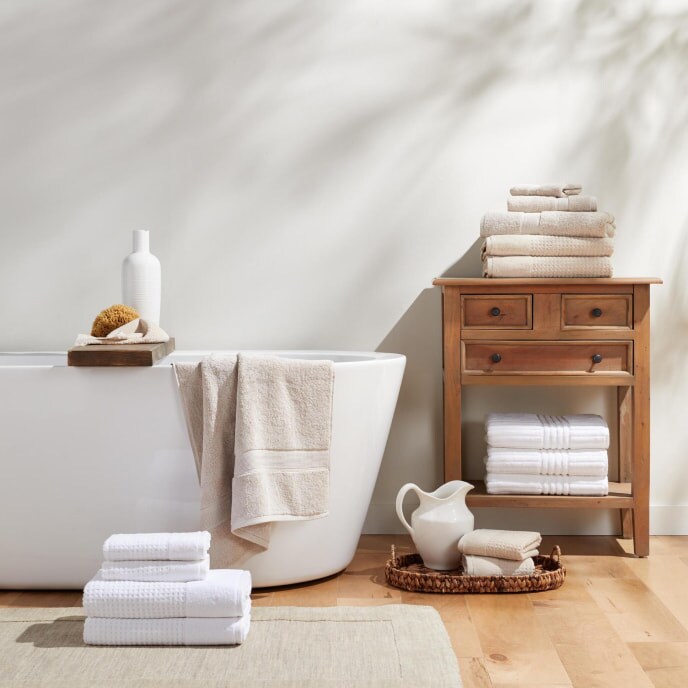 Bathroom with modern tub, white & beige towels, and wooden side table.
