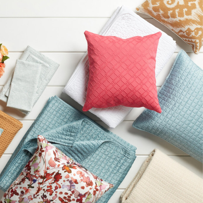Overhead shot of folded blankets and pillows in shades of blue, orange, white, and pink.