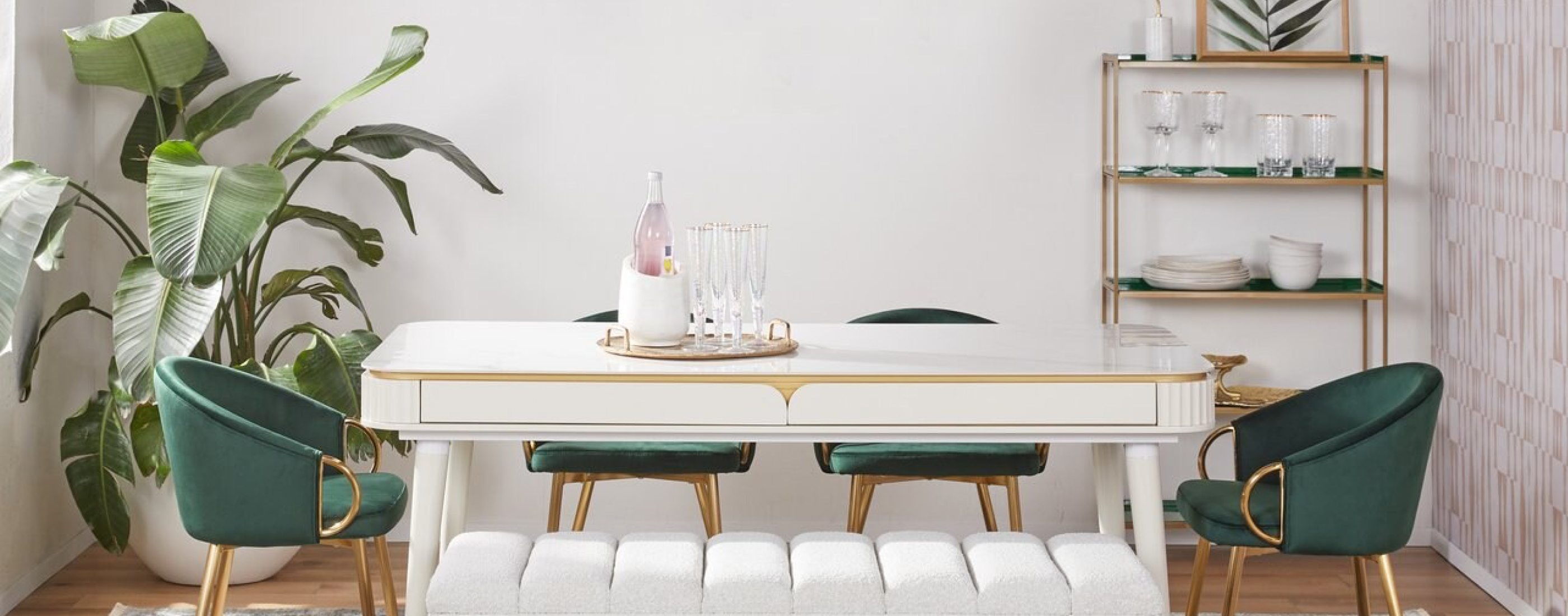 A glam dining room with a white dining rectangular table, green velvet chairs, and a padded white bench on one side.