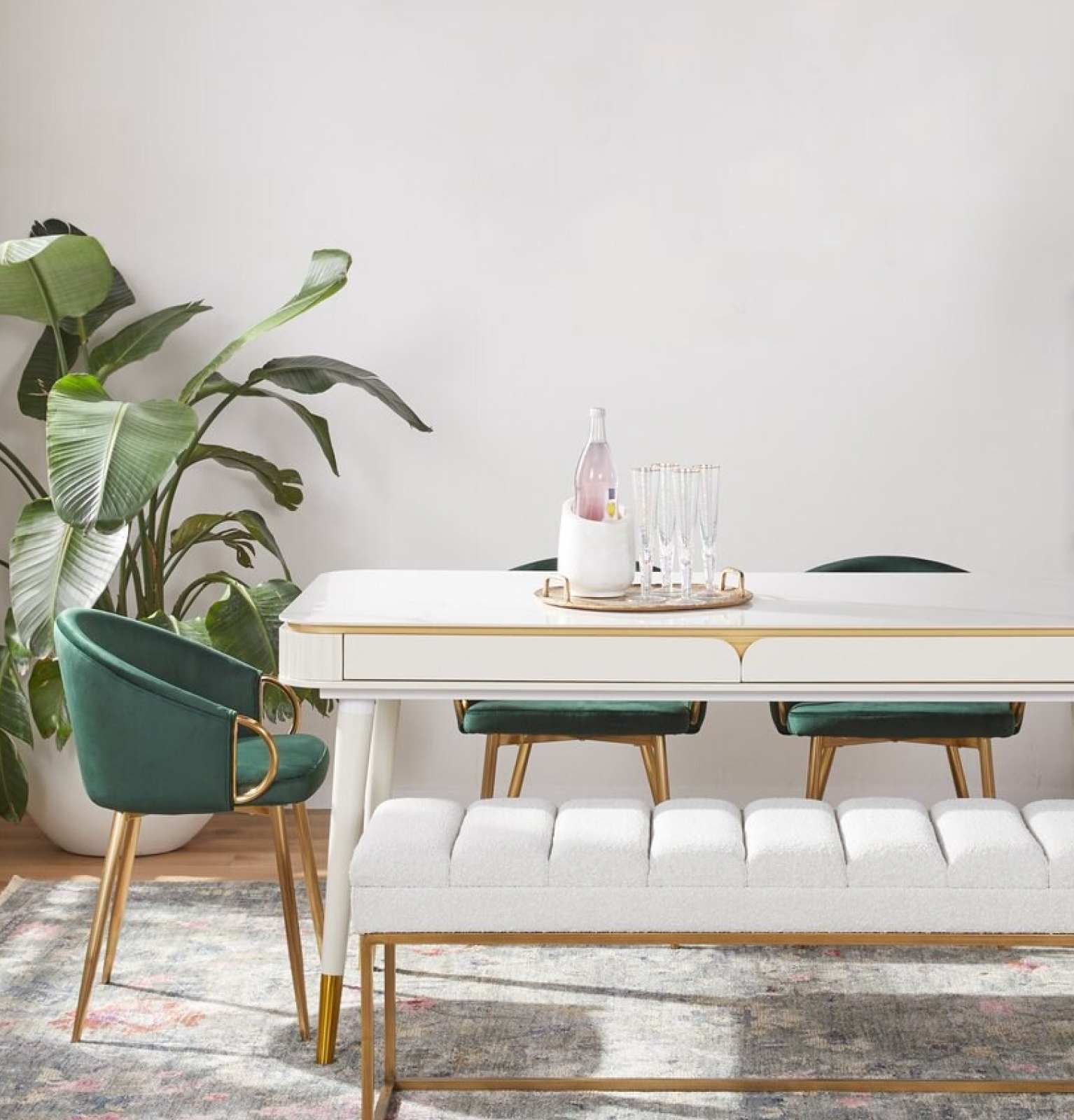 A glam dining room with a white dining rectangular table, green velvet chairs, and a padded white bench on one side.