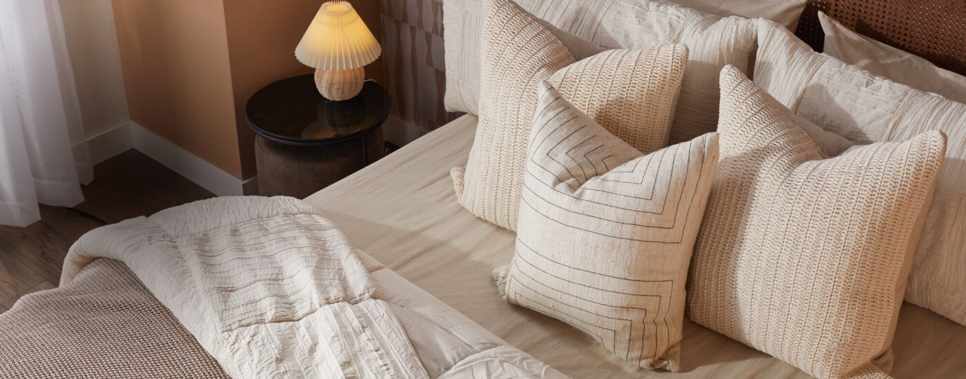 A bed with beige bedding, turned down with plush pillows and a thick comforter.