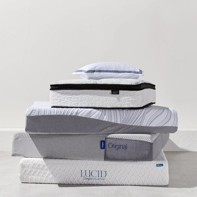An off-center stack of mattresses in multiple sizes, topped with a pillow.