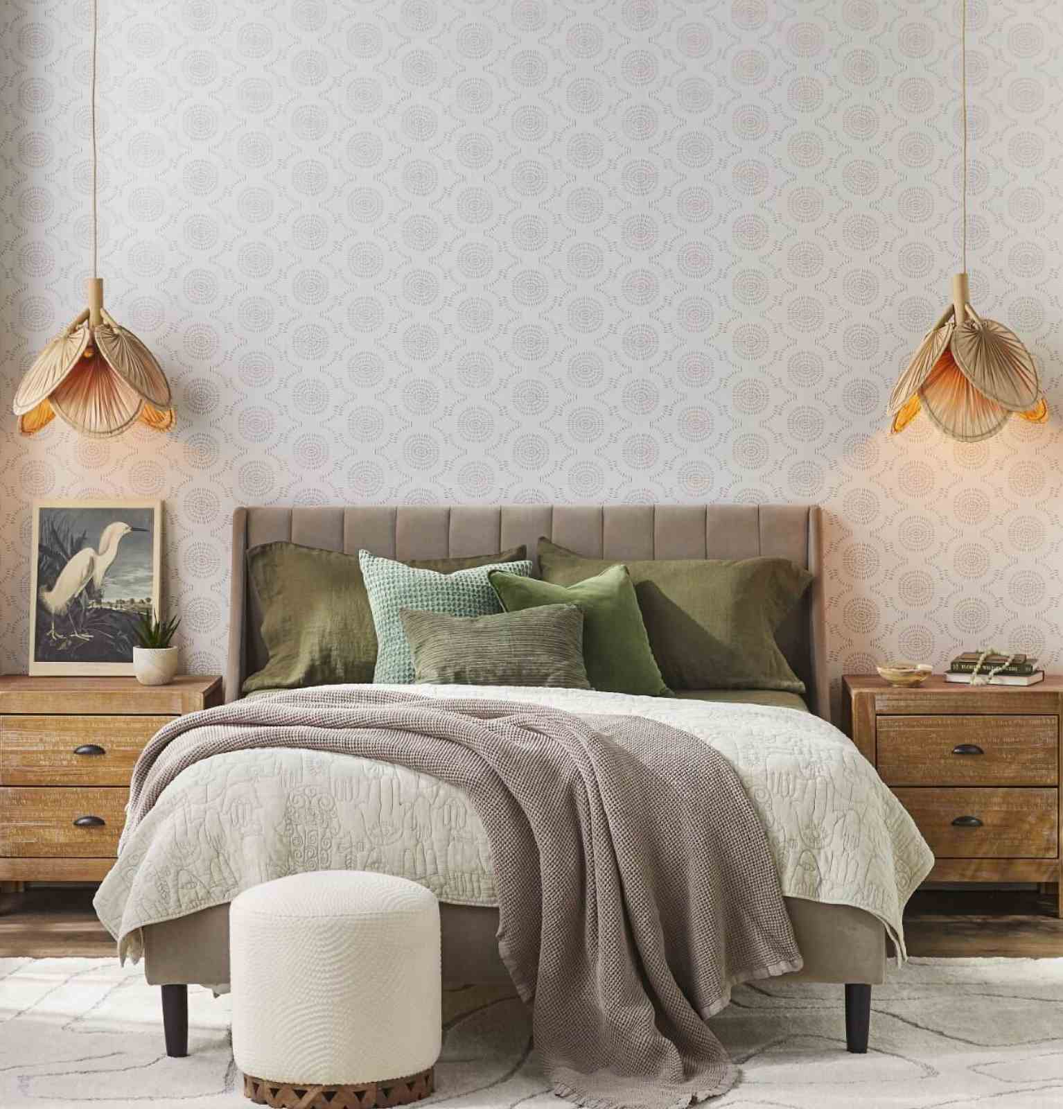 Coastal-style bedroom with natural wood nightstands, mattress layered with cozy blankets and pillows, and a tufted taupe velvet headboard.