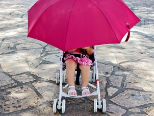 Little girl with a pink umbrella in an umbrella stroller