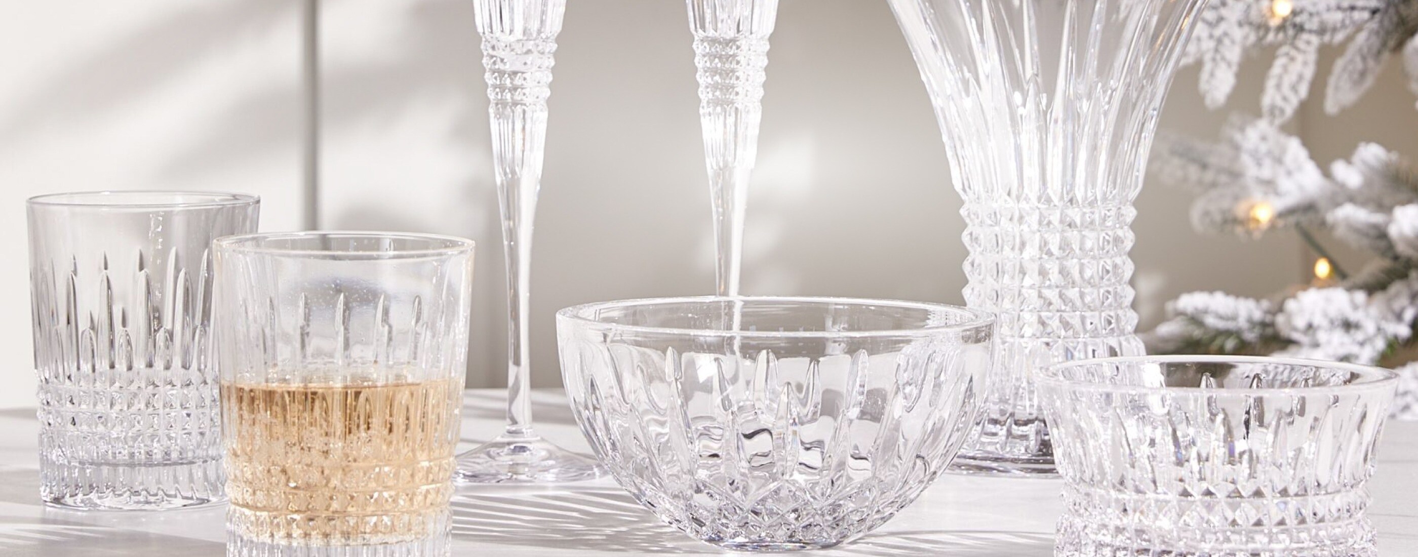 A closeup display of crystal bowls, tumblers, champagne flutes, and vases on a white tablecloth.