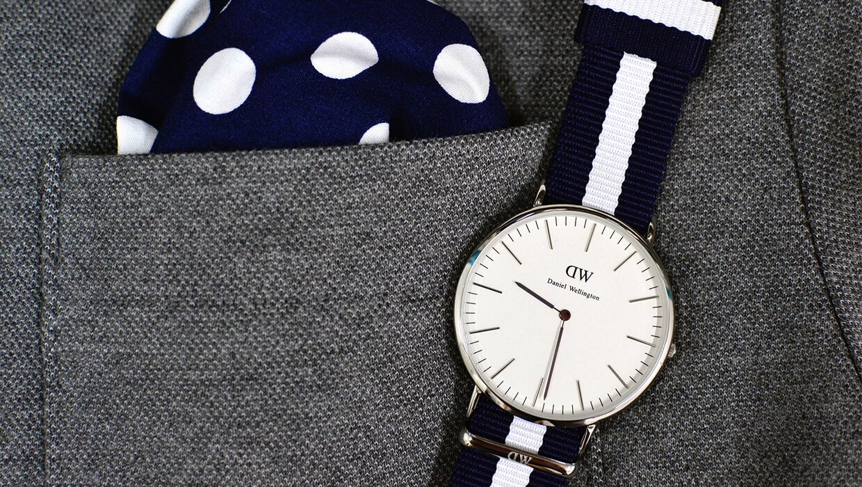 Close up of a watch laying on a suit jacket next to a navy and white pocket square