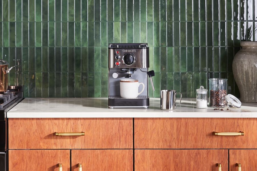Espresso machine on a counter in a kitchen with a green backsplash
