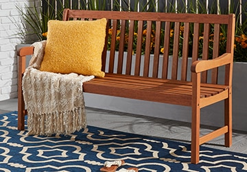 Wooden outdoor bench with a pillow and throw on a blue rug