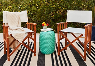 Turquoise accent table between two outdoor chairs in front of a hedge