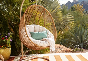 Wicker hanging chair with a plush cushion and a throw