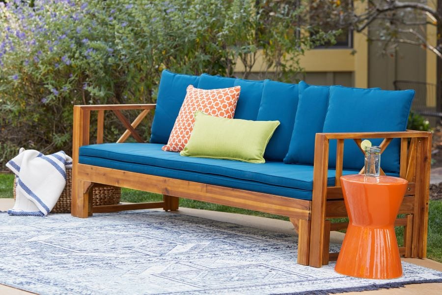 Orange hourglass side table by outdoor sofa with blue cushions