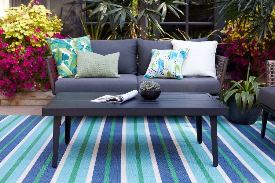 Wicker loveseat with blue cushions over a blue, white, and green striped run