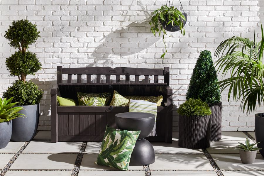 Storage bench holding green cushions on patio with topiaries