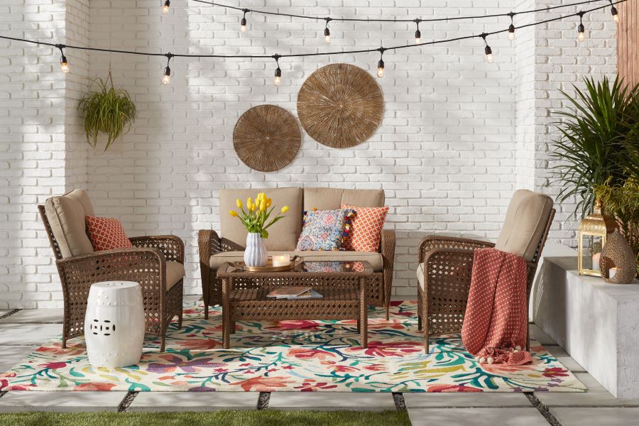 Wicker patio set with tan cushions on a colorful rug and beneath string lights